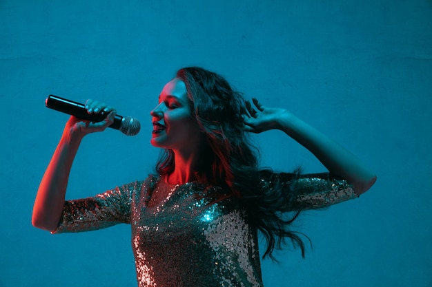 Retrato de cantante femenina aislado en la pared azul del estudio en luz de neón