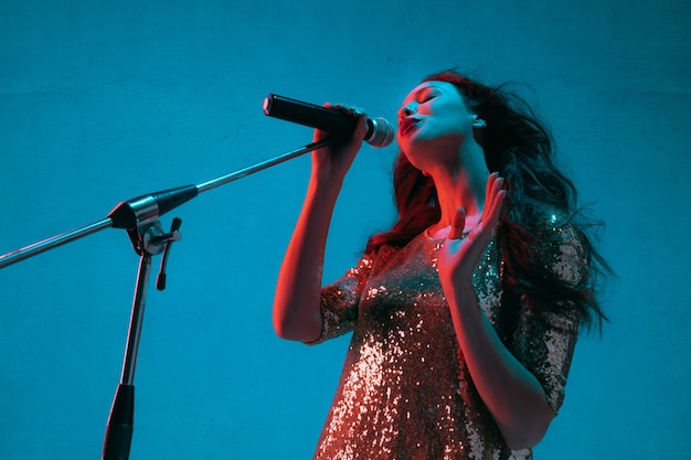 Retrato de cantante femenina aislado en la pared azul del estudio en luz de neón