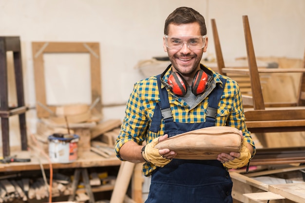 Retrato de carpintero hombre sonriente sosteniendo modelo de madera incompleta