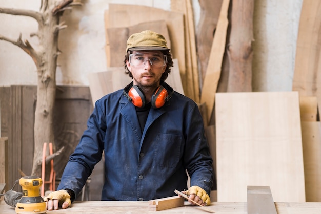 Foto gratuita retrato de un carpintero macho con gafas de seguridad de pie detrás de la mesa de trabajo