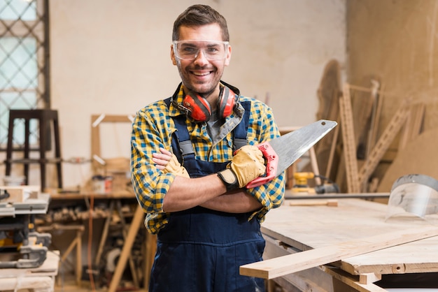 Retrato de un carpintero de sexo masculino sonriente que sostiene el handsaw que mira la cámara