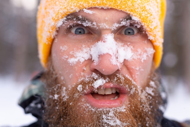 Un retrato cercano de un hombre con barba, todo rostro en la nieve, en un bosque nevado