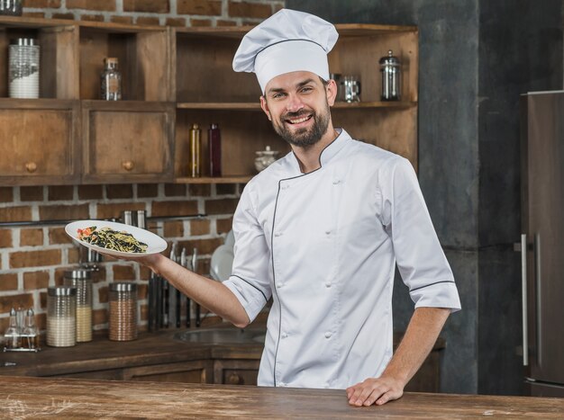 Retrato del chef masculino feliz que presenta el sabroso plato de espagueti