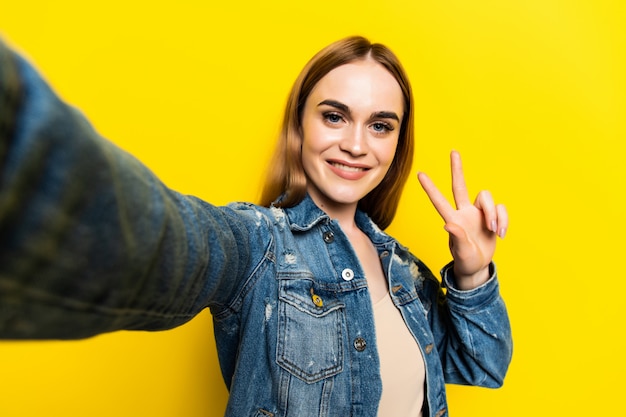 Foto gratuita retrato de chica alegre alegre disparando selfie en cámara frontal aislada en la pared amarilla