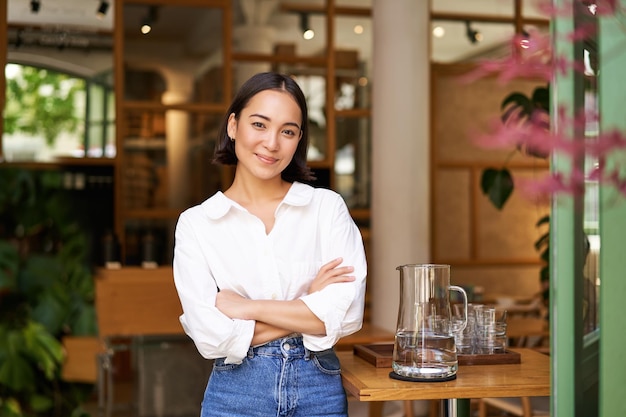 Foto gratuita retrato de una chica asiática sonriente con camisa de cuello blanco que trabaja en un café que administra un restaurante con aspecto de estafa