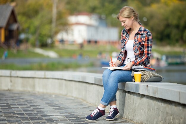 Retrato de una chica atractiva estudiante sentado en la escritura del puente