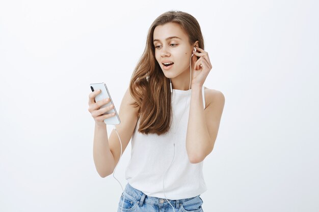Retrato de chica atractiva moderna poner auriculares, escuchar podcast o música en el teléfono móvil
