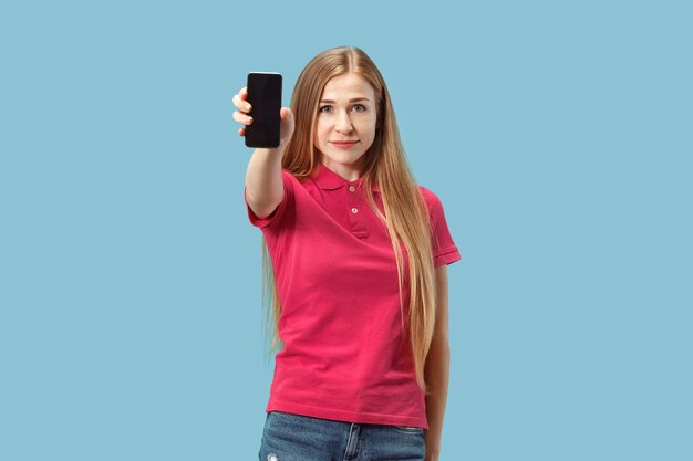 Retrato de una chica casual segura que muestra el teléfono móvil de pantalla en blanco aislado sobre fondo azul.