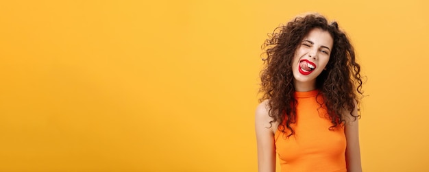 Retrato de una chica caucásica alegre, juguetona y elegante con cabello rizado y lápiz labial rojo guiñando un ojo showi