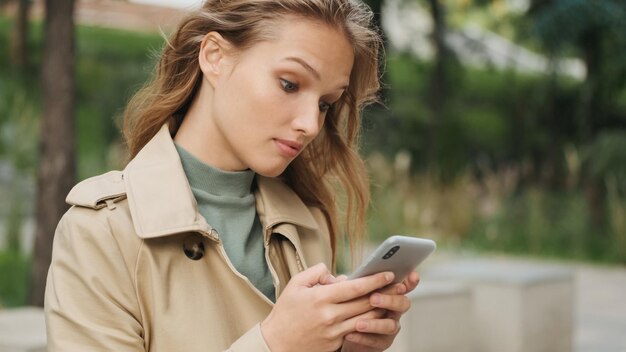 Retrato de una chica elegante que parece sorprendida respondiendo mensajes en un teléfono inteligente al aire libre Estudiante femenina descansando en el parque