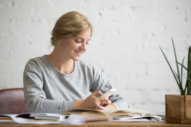 Retrato de una chica de estudiante en el escritorio con el teléfono