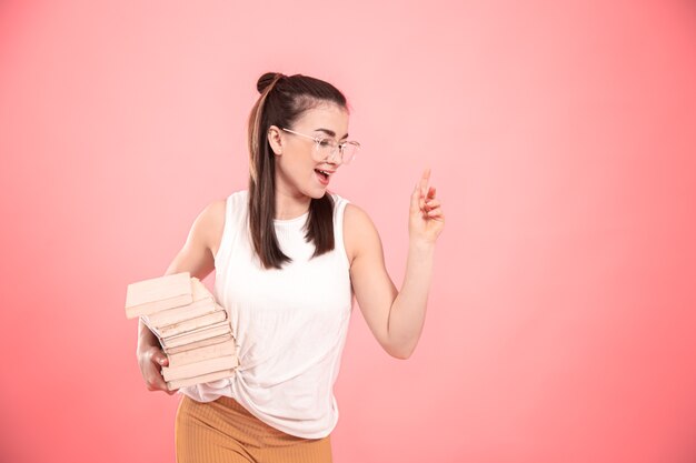 Retrato de una chica estudiante con gafas sobre un fondo rosa con libros en sus manos. Concepto de educación y aficiones.