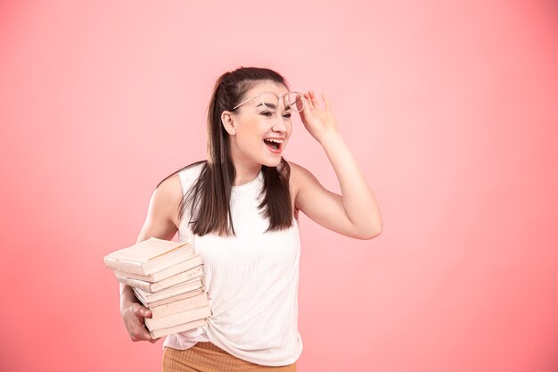 Retrato de una chica estudiante con gafas sobre un fondo rosa con libros en sus manos. Concepto de educación y aficiones.