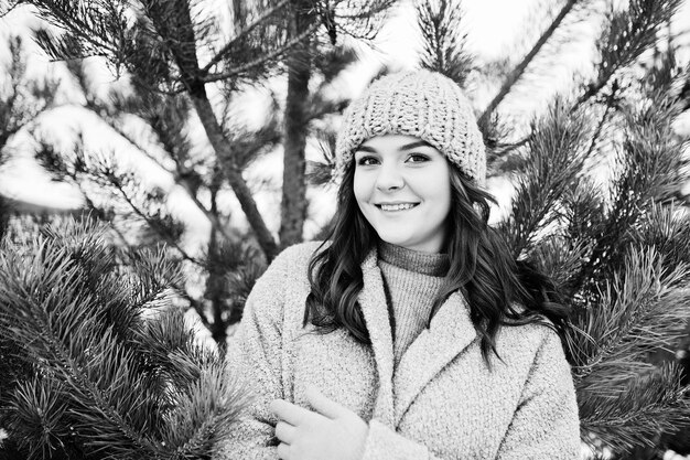 Retrato de una chica gentil con abrigo gris y sombrero contra el árbol de año nuevo al aire libre