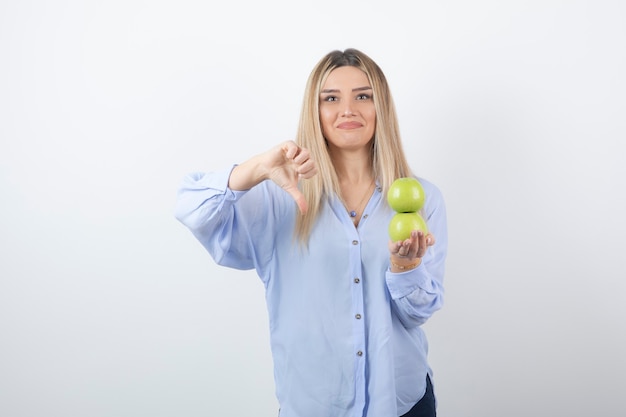 Retrato de una chica guapa modelo sosteniendo manzanas frescas y mostrando un pulgar hacia abajo.