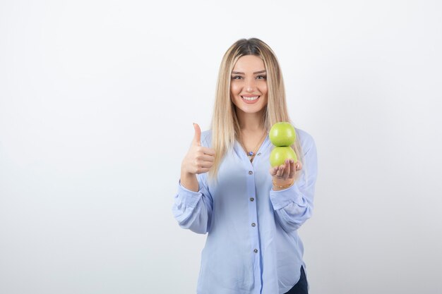Retrato de una chica guapa modelo sosteniendo manzanas frescas y mostrando un pulgar hacia arriba.