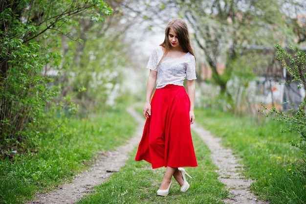 Retrato de una chica hermosa con labios rojos en el jardín de flores de primavera con vestido rojo y blusa blanca