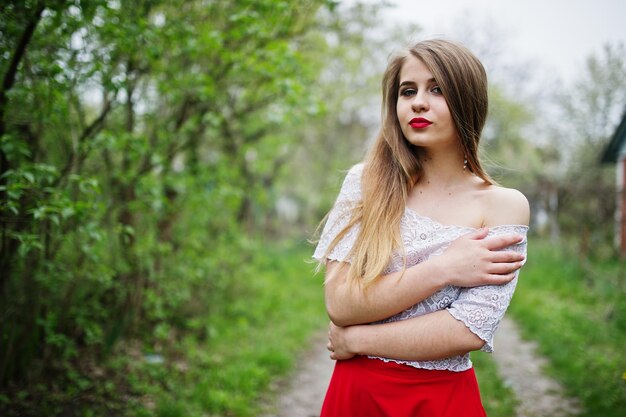 Retrato de una chica hermosa con labios rojos en el jardín de flores de primavera con vestido rojo y blusa blanca