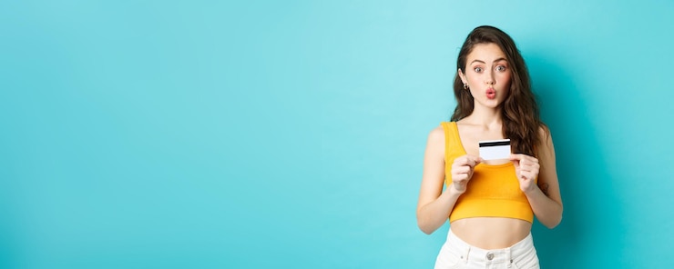 Foto gratuito retrato de una chica hermosa sorprendida que parece divertida y labios fruncidos que muestran una tarjeta de crédito de plástico contra un fondo azul