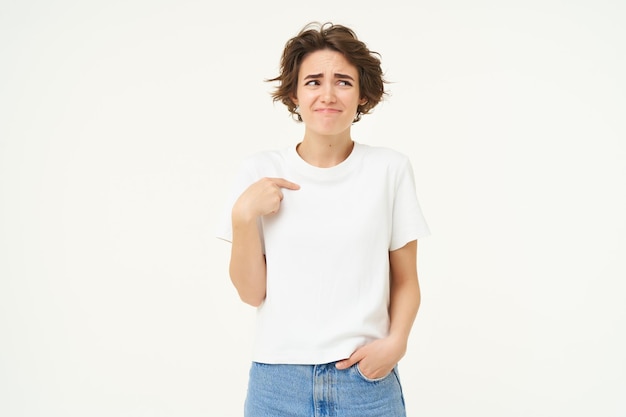 Foto gratuita retrato de una chica incómoda que se siente incómoda apuntándose a sí misma con cara insegura posando