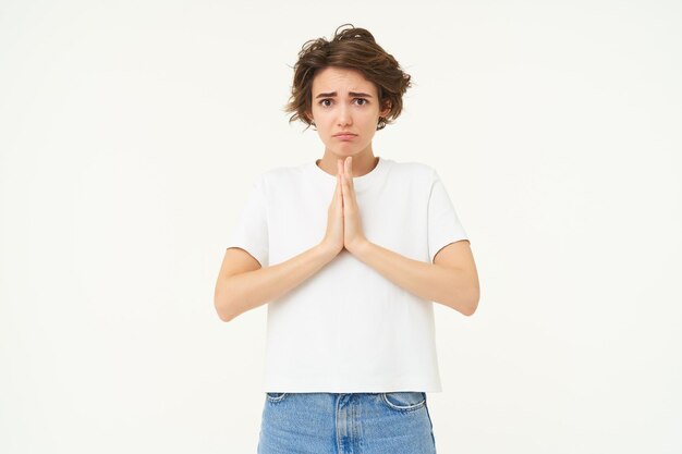 Retrato de una chica mirando con cara de mendicidad tomándose de la mano en oración suplicando pidiendo deseo de pie