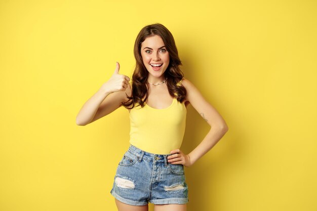 Retrato de una chica moderna con estilo, una mujer femenina mostrando su aprobación, recomendando gestos, gustar o aprobar, elogiar, de pie sobre un fondo amarillo