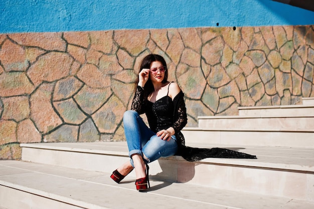 Retrato de una chica morena con gafas rosas puestas en negro al aire libre en un día soleado