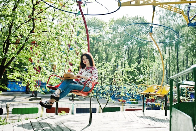 Retrato de una chica morena con gafas rosas y sombrero con helado en el parque de atracciones