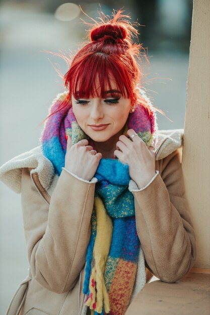 Retrato de una chica pelirroja con flequillo sosteniendo su bufanda colorida