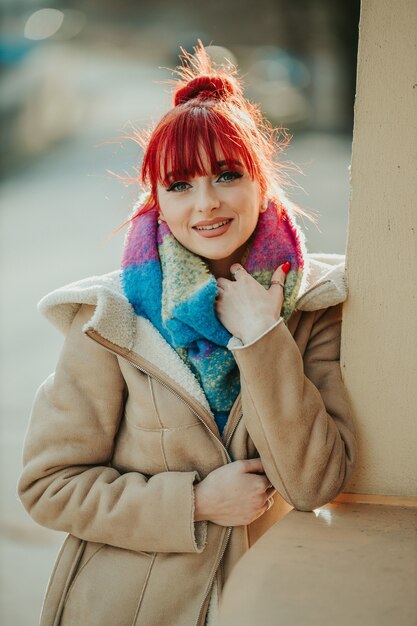 Retrato de una chica pelirroja con flequillo sosteniendo su bufanda colorida