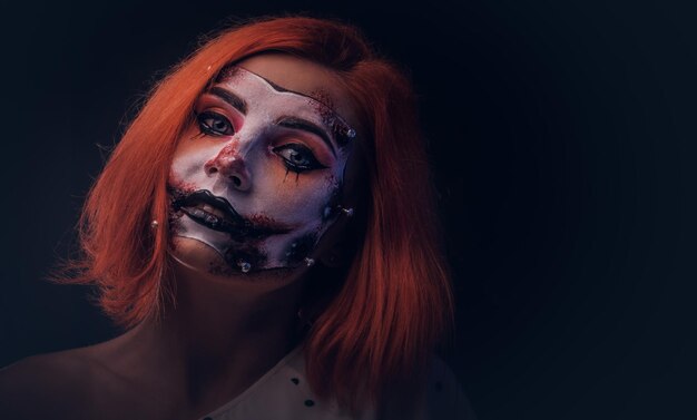 Retrato de una chica pelirroja con maquillaje espeluznante para Halloween en un estudio fotográfico oscuro.