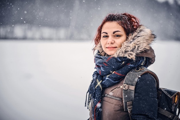 Retrato de una chica pelirroja con una mochila caminando por el bosque de invierno
