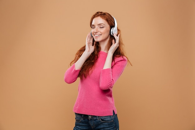Retrato de una chica pelirroja sonriente satisfecha escuchando música con auriculares