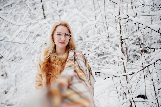 Retrato de una chica rubia con gafas, abrigo de piel rojo y bufanda en el día de invierno