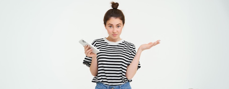 Foto gratuito el retrato de una chica sorprendida se encoge de hombros y parece una reacción confusa ante algo que vio en el móvil