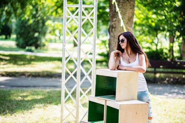 Retrato de una chica vestida a la moda posando en cajas de madera en el parque en un día soleado