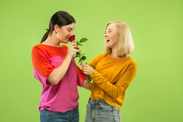 Retrato de chicas muy encantadoras en trajes casuales aislados sobre fondo verde de estudio. Dos modelos femeninas como novias o lesbianas. Concepto de LGBT, igualdad, emociones humanas, amor, relación.