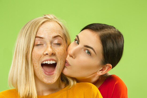 Retrato de chicas muy encantadoras en trajes casuales aislados sobre fondo verde de estudio. Dos modelos femeninas como novias o lesbianas. Concepto de LGBT, igualdad, emociones humanas, amor, relación.