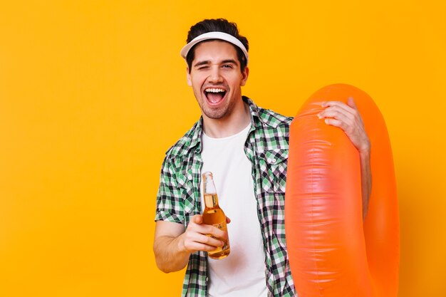 Retrato de chico brunet con gorra blanca apuntando a la cámara. Hombre con anillo de goma con cerveza.