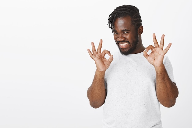 Retrato de chico feliz con trenzas posando contra la pared blanca