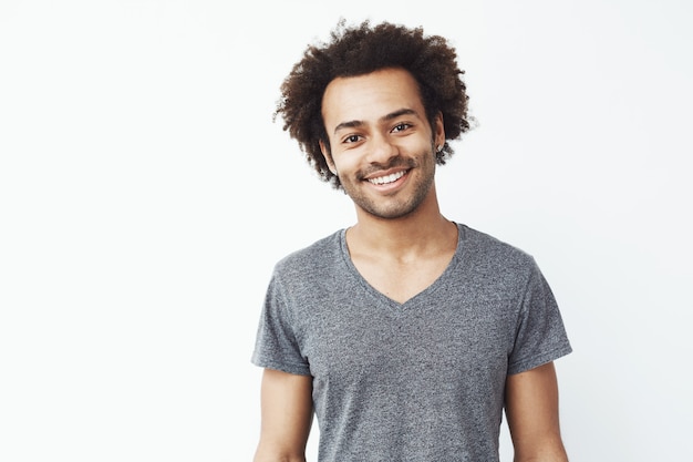 Retrato de chico guapo africano sonriendo sobre pared blanca. Estudiante seguro o joven empresario.