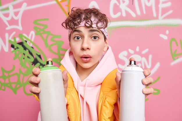 Retrato de un chico guapo hipster de pelo rizado sorprendido que usa aerosol para dibujar marcas de graffiti.