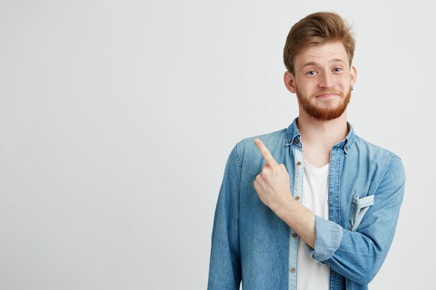 Retrato de chico guapo joven alegre sonriente apuntando el dedo hacia arriba.