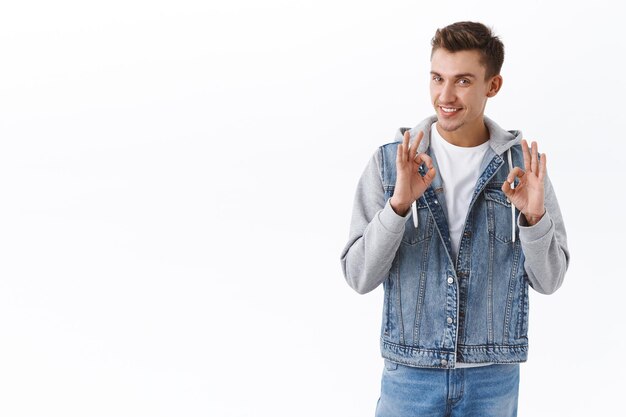 Retrato de chico guapo seguro que asegura la mejor calidad del producto, muestra signos de bien y sonríe