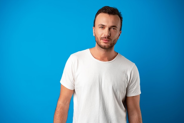 Retrato de chico guapo sonriente en camiseta blanca sobre fondo azul.