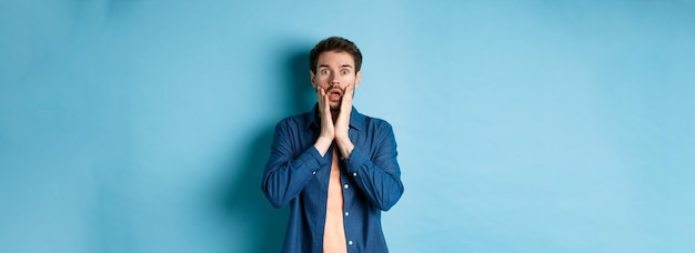 Foto gratuita retrato de chico jadeando y dejando caer la mandíbula con la cara conmocionada mirando a la cámara sorprendido de pie en bl