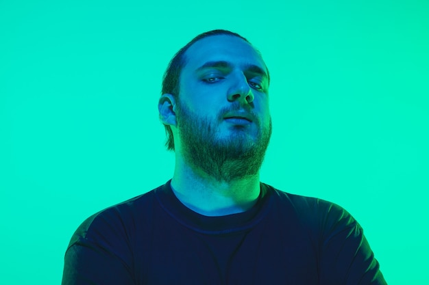 Retrato de un chico con luz de neón de colores en la pared verde. Modelo masculino con estado de ánimo tranquilo y serio. Expresión facial, estilo de vida y apariencia de los millenials. Futuro, tecnologías.