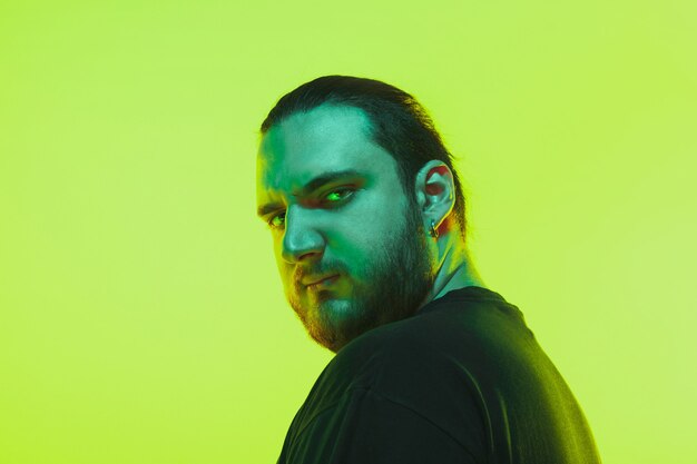 Retrato de un chico con luz de neón de colores en la pared verde. Modelo masculino con estado de ánimo tranquilo y serio. Expresión facial, estilo de vida y apariencia de los millenials. Futuro, tecnologías.