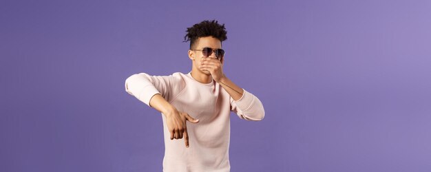 Retrato en la cintura de un chico guapo joven y genial con rastas gafas de sol en espera con la mano sobre la boca mientras bea