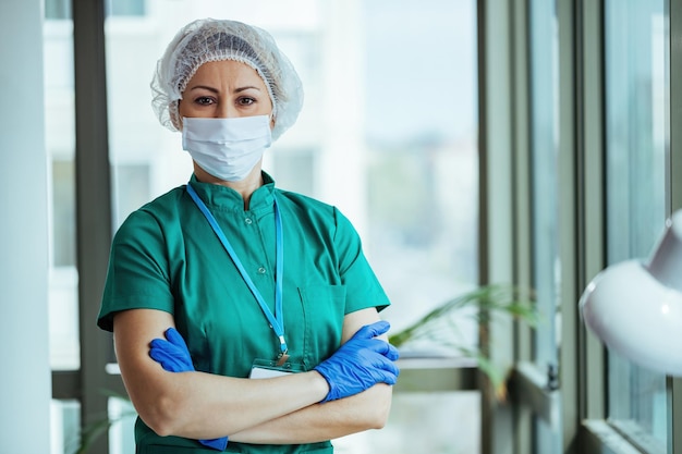 Retrato de cirujano de pie con los brazos cruzados en la clínica médica y mirando a la cámara